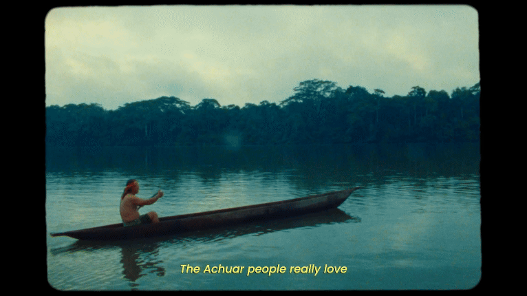 a gif from the short documentary film 'I Am the Nature' featuring an Indigenous Achuar man paddling a canoe in a river, with subtitle text reading "The Achuar people really love the wy of living in this part of the world."