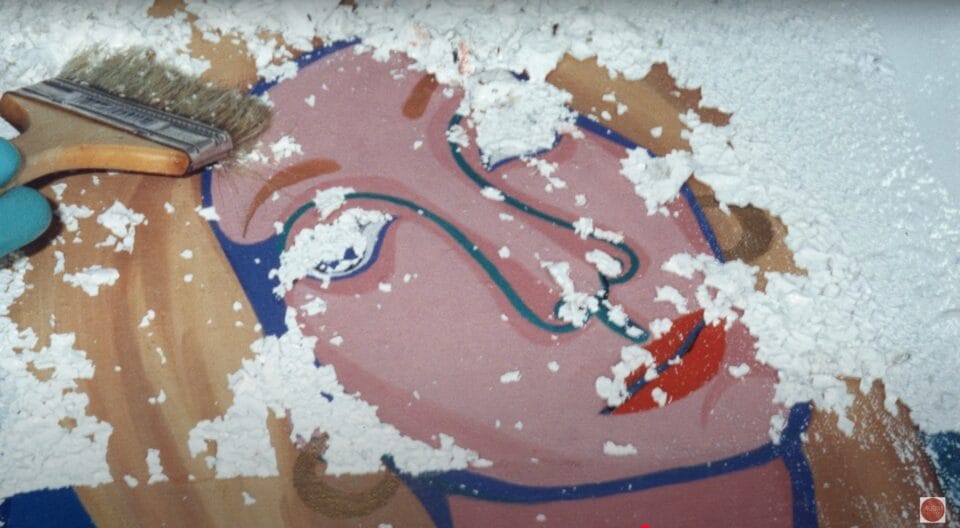 a video still of a restorer uncovering a woman's face