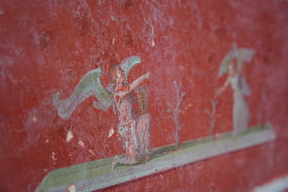 a detail of a large-scale fresco uncovered in Pompeii inside of a banquet hall, depicting small figures on a red background