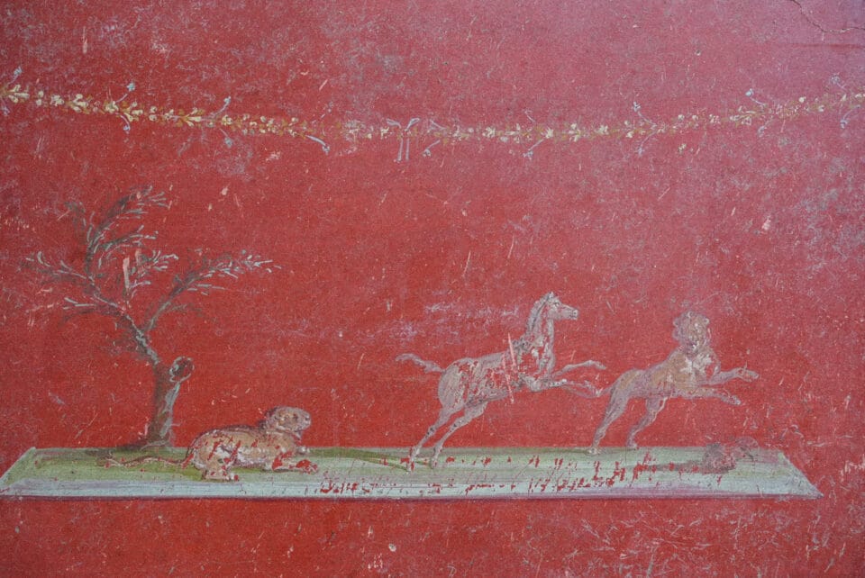 a detail of a large-scale fresco uncovered in Pompeii inside of a banquet hall, depicting horses on a red background