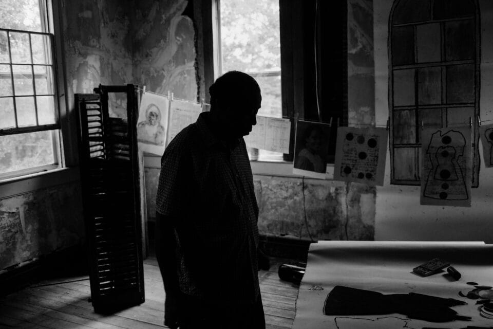 a black and white image of the artist working on tables in a dilapidated antebellum mansion