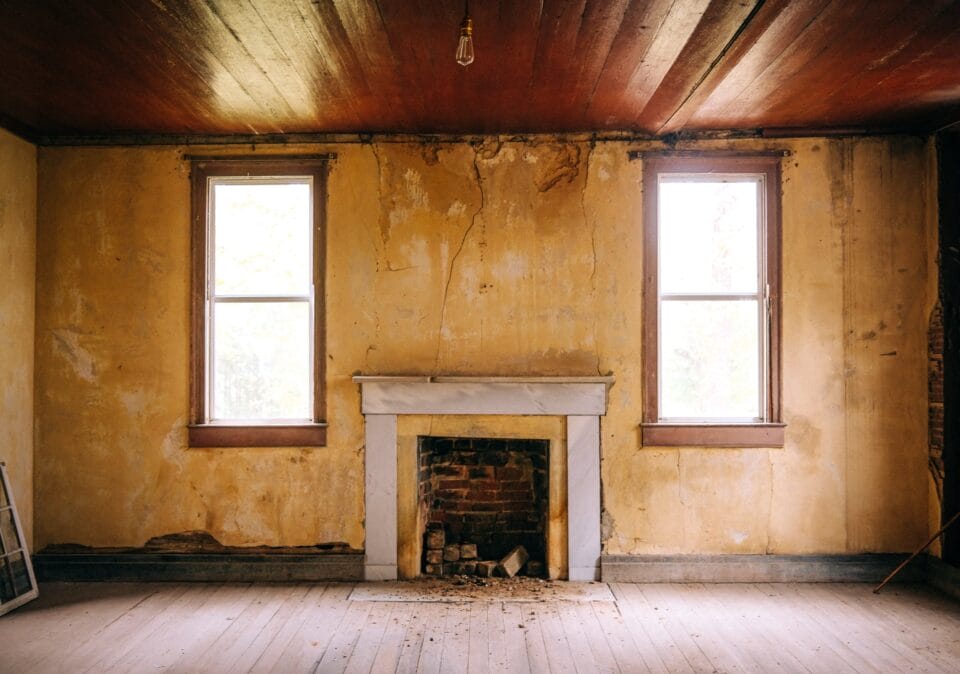 the interior of an antebellum mansion with peeling walls and a fireplace