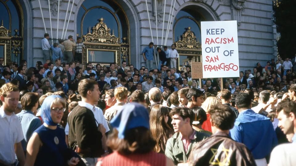 a photo of people at a demonstration. one holds up a sign that says "keep racism out of san francisco"